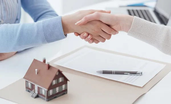 Hình ảnh bắt tay và mô hình nhà thể hiện quá trình giao dịch pháp lý, phù hợp với nội dung về hợp đồng và thủ tục