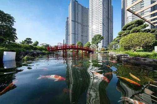 Một chiếc thuyền nhỏ neo gần bến, mặt nước lăn tăn dưới nắng sớm, phía sau là hàng cây xanh tạo cảm giác dịu nhẹ của công viên ven sông Vinhomes