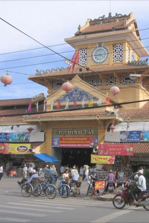 ảnh ngôi chợ trăm tuổi nhìn xéo từ góc đường, mái ngói đỏ và tường vàng nổi bật dưới trời xanh, vài xe máy dừng lại khiến khung hình mang nét đẹp hoài niệm nhẹ nhàng