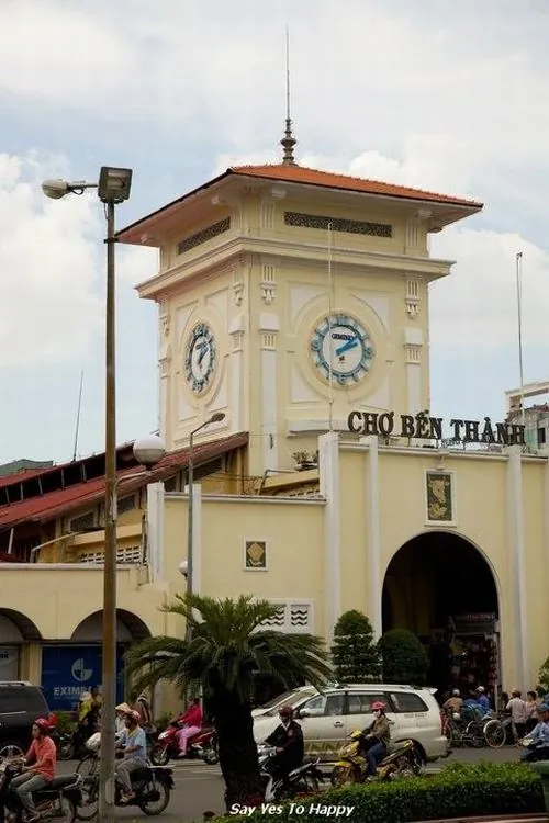 ảnh biểu tượng Sài Gòn ghi lại mặt tiền chính với người qua lại đông đúc, vài chiếc xe buýt và taxi dừng đón khách, không khí tấp nập nhưng vẫn giữ nét cổ kính