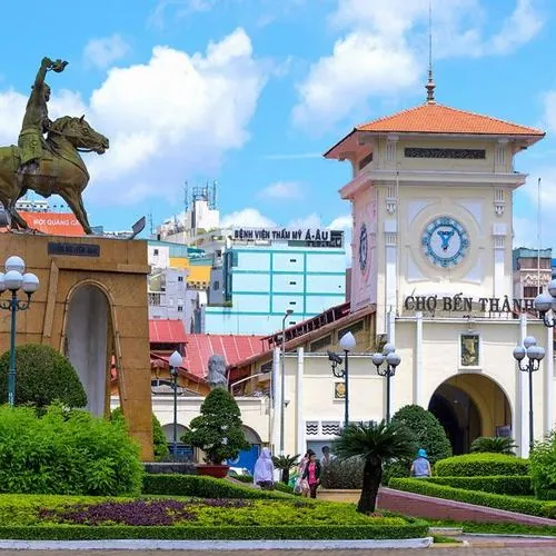 Từ khoảng sân rộng, cổng chợ hiện ra với gam vàng ấm, người dân đi bộ thong thả, bối cảnh này làm nổi bật linh hồn của đất Sài Thành trong buổi sáng sớm