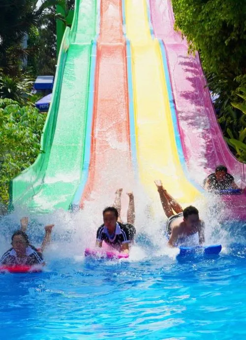 Hai làn trượt song song sắc màu nổi bật, từng nhóm bạn nằm sấp lao xuống hồ tạo sóng, gương mặt cười tươi giữa không khí náo nhiệt cuối tuần