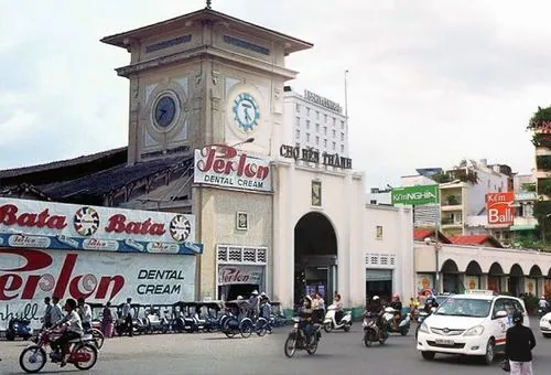 Góc đường nhỏ gần chợ, một người đàn ông ngồi uống cà phê, nhìn dòng xe qua lại như đang ngắm lại nhịp sống quen thuộc của thành phố