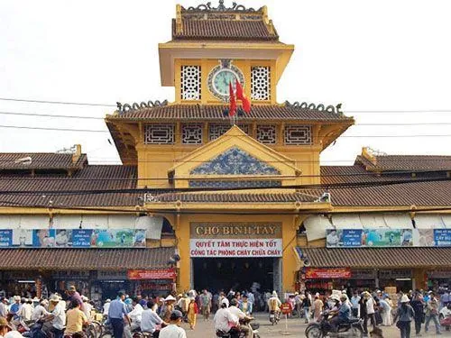 Một người thợ may đang cặm cụi bên chiếc máy cũ, xung quanh treo đầy vải vóc đủ màu, không gian nhỏ nhưng rất ấm và gần gũi