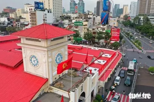 Một bác tài xích lô đứng chờ khách, tay chống lên yên xe, ánh mắt nhìn xa xăm giữa dòng người vội vã đi ngang