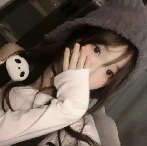 Gái đẹp dùng tay che miệng đứng trước rèm cửa, tóc đen dài buộc nơ hồng, outfit nữ tính nhẹ nhàng trong nhà.