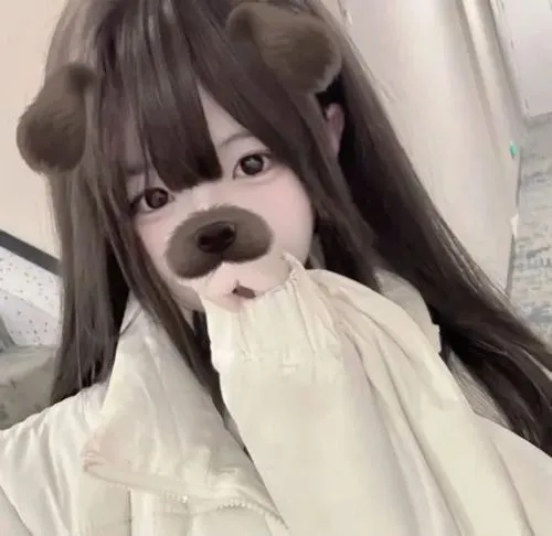 Ảnh gái xinh đội mũ lông kem kéo cao che miệng, tóc đen dài, áo len rộng ôm gối trắng, ánh mắt long lanh.