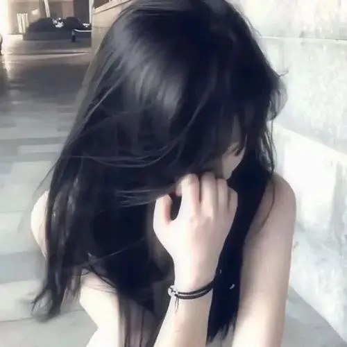 Thiếu nữ ôm gối trắng che nửa mặt, tóc nâu dài xõa, mặc áo mỏng trong phòng ngủ ấm cúng.