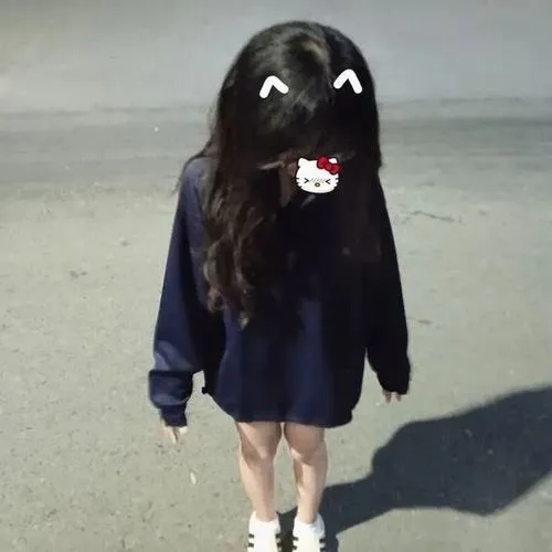 Thiếu nữ mặc hoodie đen có hoạ tiết kéo mũ che mặt, tóc đen dài, ngồi trên ghế sofa.