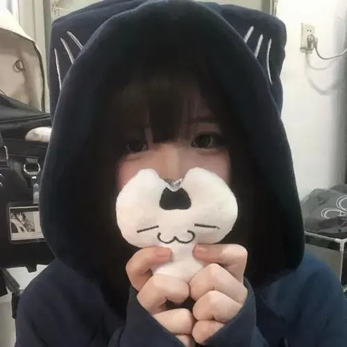 Thiếu nữ mặc hoodie đen có tai gấu ôm con gấu nhỏ che mặt, mái tóc đen dài với mái ngố, ánh sáng dịu nhẹ toát lên vẻ dễ thương.