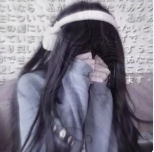 Ảnh gái xinh đội mũ len xám kéo sụp che mặt một bên, tóc đen dài rối nhẹ, hoodie rộng khoe dáng ngồi trong phòng.