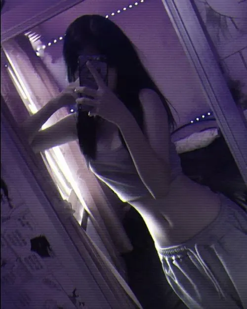 Gái xinh đứng nghiêng trong ánh tím neon mặc áo hai dây trắng bó một tay cầm điện thoại che kín mặt khoe eo thon mềm mại.