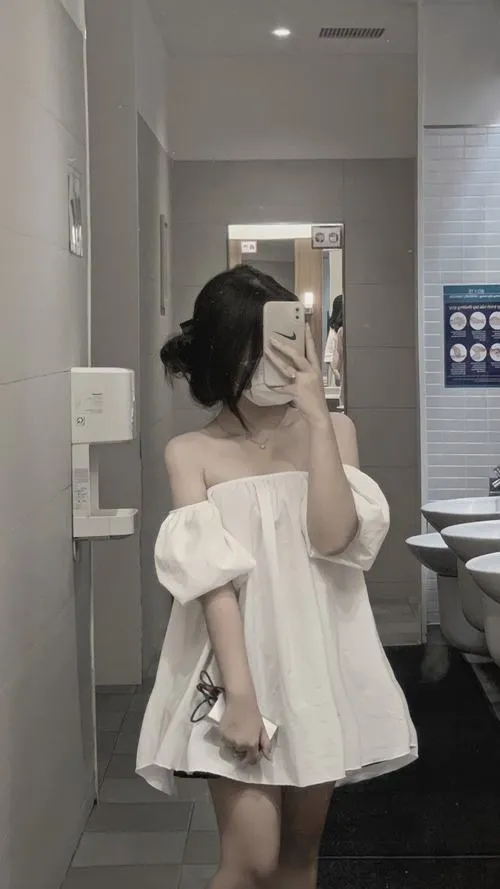Hot girl vai trần trong áo off shoulder trắng tóc búi cao cầm điện thoại che mặt trước gương soi đầy quyến rũ.