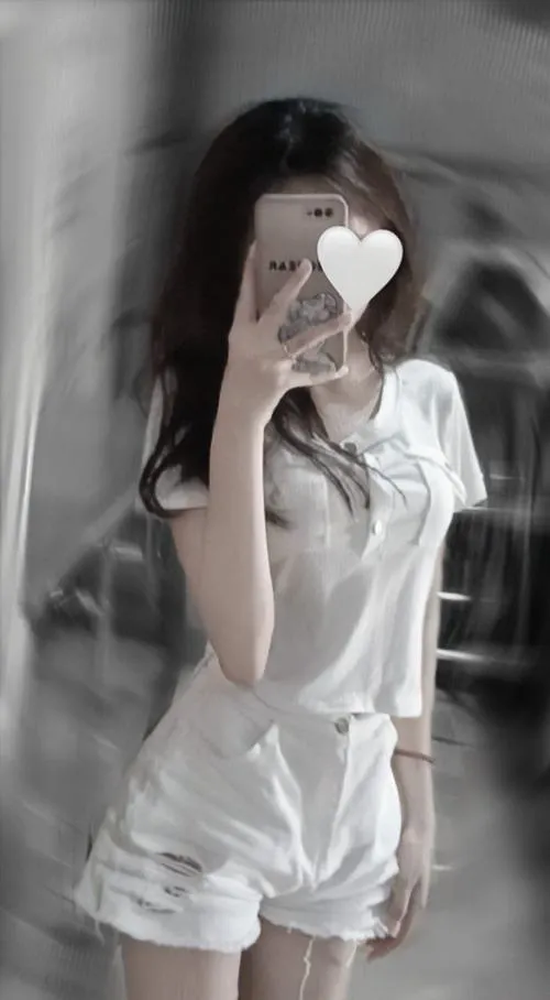 Mỹ nhân mặc áo trắng phối váy trắng cầm điện thoại dán sticker tim che mặt dưới ánh sáng dịu.
