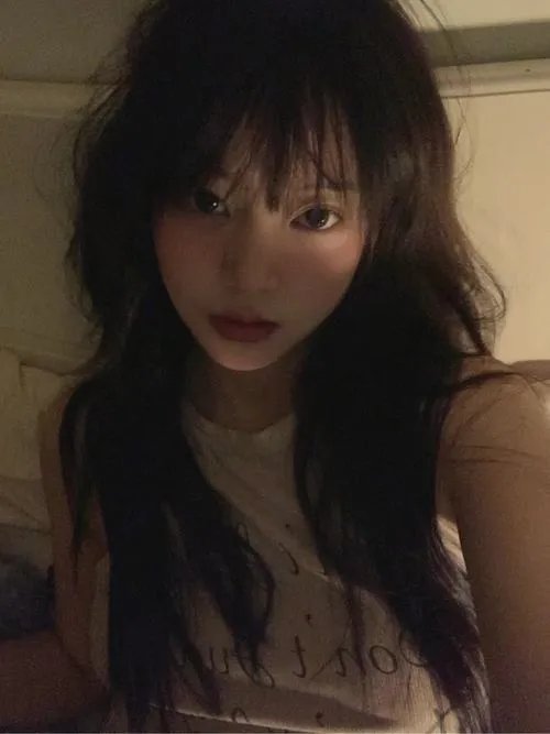 Ảnh gái xinh tóc dài đen đang nhìn nghiêng nhẹ vào ống kính với nụ cười e ấp, áo trắng mỏng khoe vai tròn trong ánh sáng dịu.