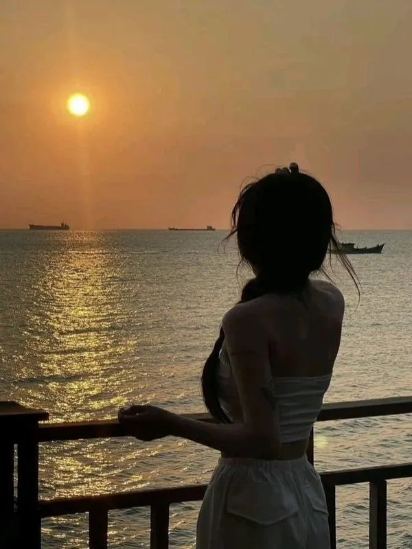 Gái đẹp quay lưng ngồi trên cát hoàng hôn mặc váy trắng ngắn tay che mặt tóc dài óng ả.