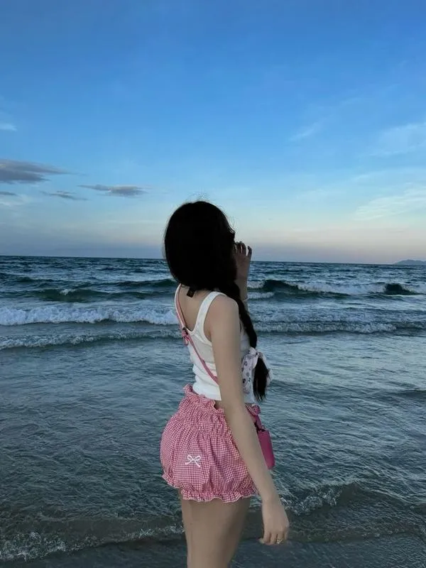 Hot girl mặc váy maxi trắng ngồi trên cát ven sóng che mặt bằng tay tóc dài bay gió.