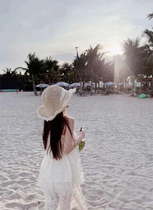 Ảnh gái quay lưng thả dáng trên đá ven biển mặc bikini đen tay vuốt tóc dài nắng vàng rực.