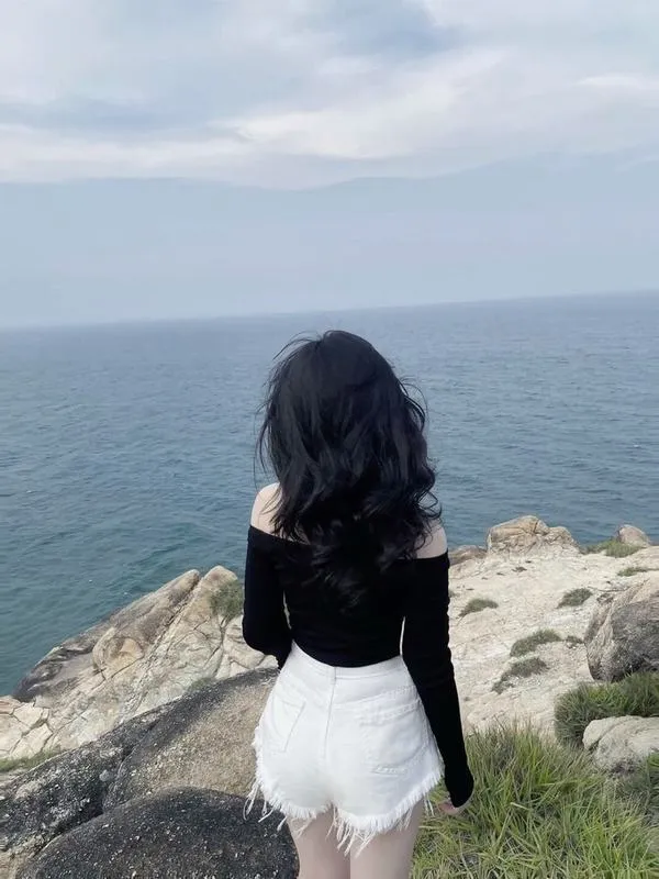 Hot girl che mặt bằng tay ngồi co chân trên cát vàng mặc áo croptop trắng nhìn ra biển.