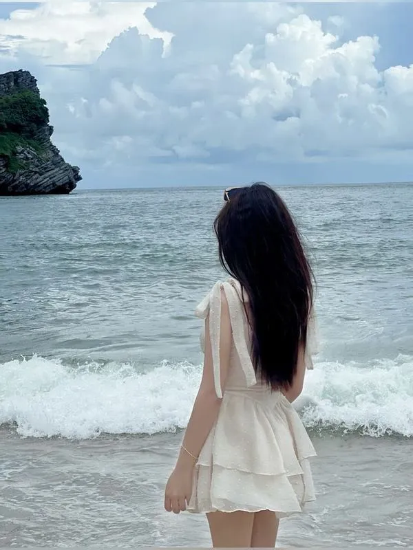 Gái đẹp đứng trên tảng đá mặc váy trắng ngắn tay nâng tóc gió thổi bay nhẹ nhàng.