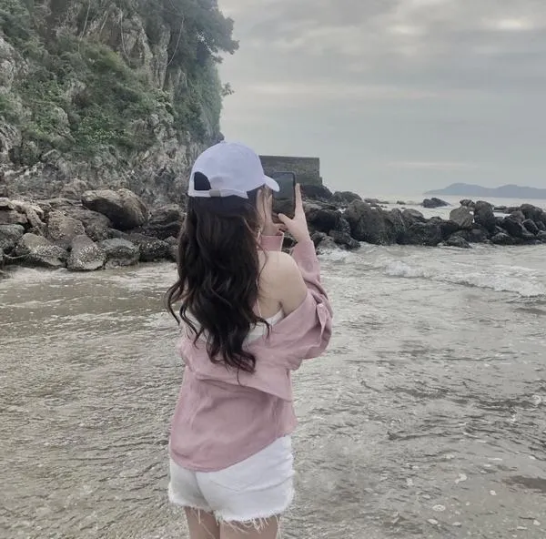 Mỹ nhân ẩn danh đi biển ngồi quay lưng mặc váy trắng dài tay che mặt bên bờ biển chiều.