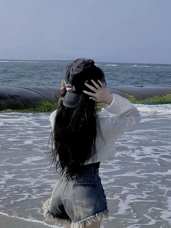 Hot girl mặc bikini trắng ngồi xổm trên cát ven sóng che mặt bằng tay tạo dáng thanh thoát.