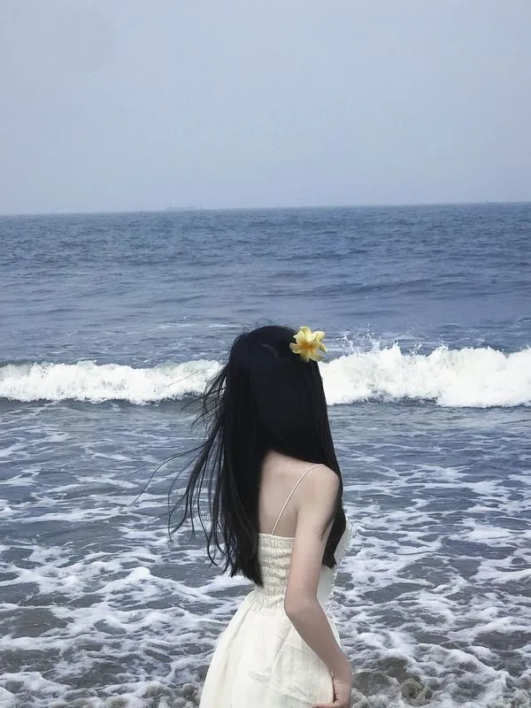 Gái đẹp ngồi co chân trên bãi đá mặc áo hai dây đen tay che mặt tóc dài đen óng.