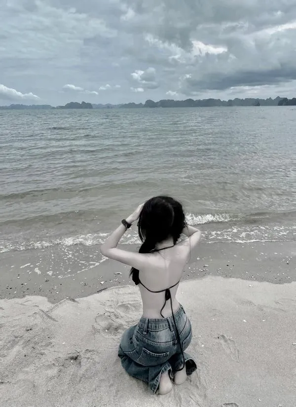 Ảnh gái quay lưng thả dáng trên bãi cát mặc váy trắng ngắn tay vuốt tóc gió biển thổi mạnh.