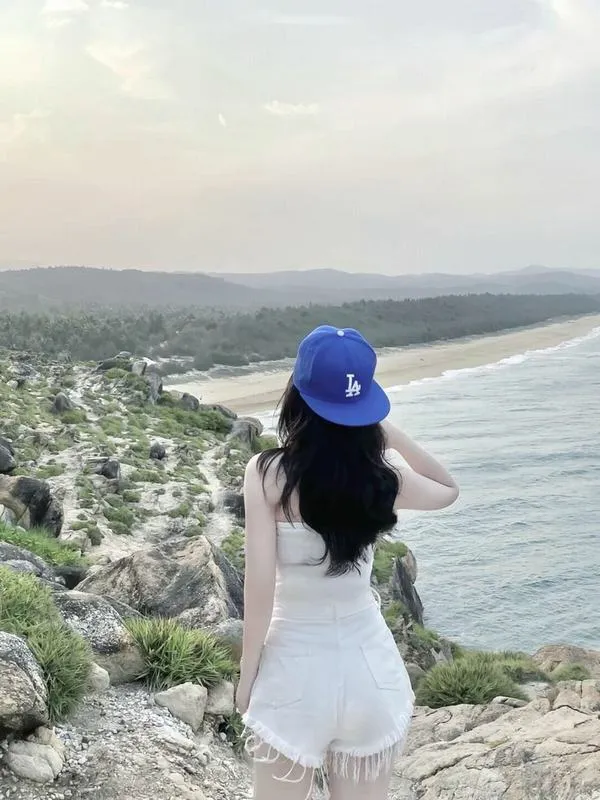 Gái xinh đứng nghiêng trên tảng đá lớn mặc áo hoodie trắng ngắn quần jeans thả dáng tự nhiên.