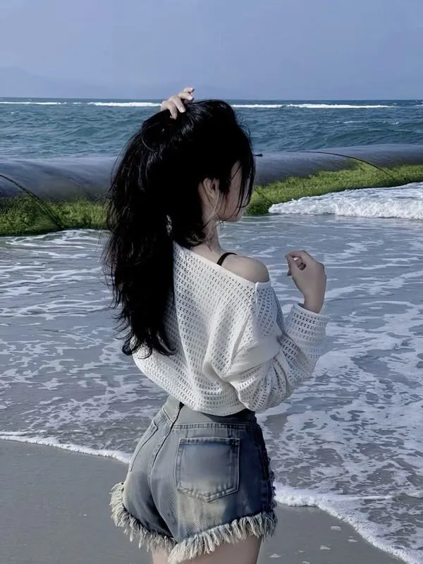 Ảnh gái đứng quay lưng trên bãi đá mặc bikini đen tay vuốt tóc dài nhìn ra biển xanh ngắt.