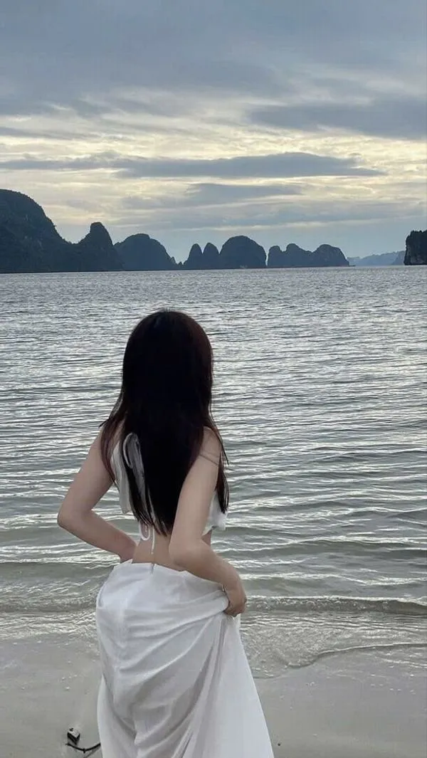 Người đẹp giấu mặt bên bờ cát ngồi quay lưng mặc váy maxi trắng tay nâng tóc dưới ánh chiều tà.