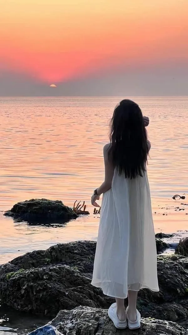 Hot girl mặc áo trắng ngắn ngồi co chân trên bãi đá nhìn hoàng hôn tóc dài đen óng ánh.