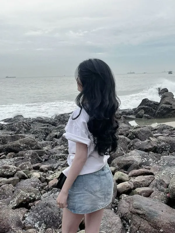 Hot girl che mặt bằng tóc ngồi bên hoàng hôn trên bãi cát mặc váy trắng dài tay cầm cát chơi.