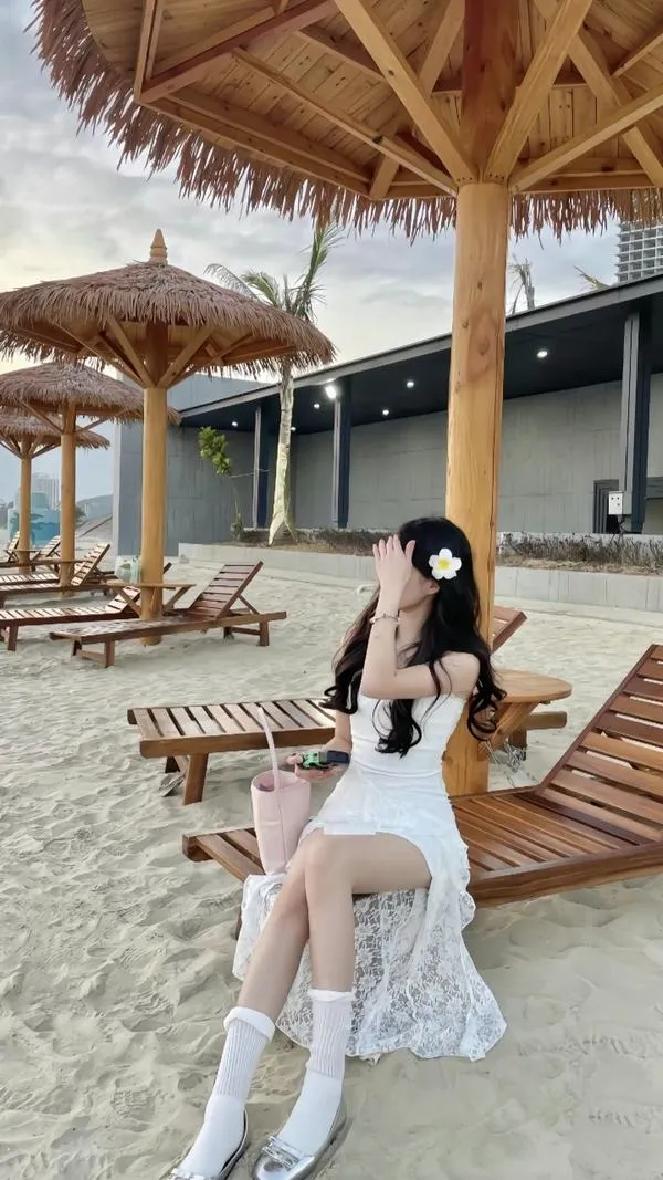 Gái xinh ngồi xổm trong nước biển nông mặc váy trắng bồng bềnh tay khẽ chạm nước tạo dáng mộng mơ.