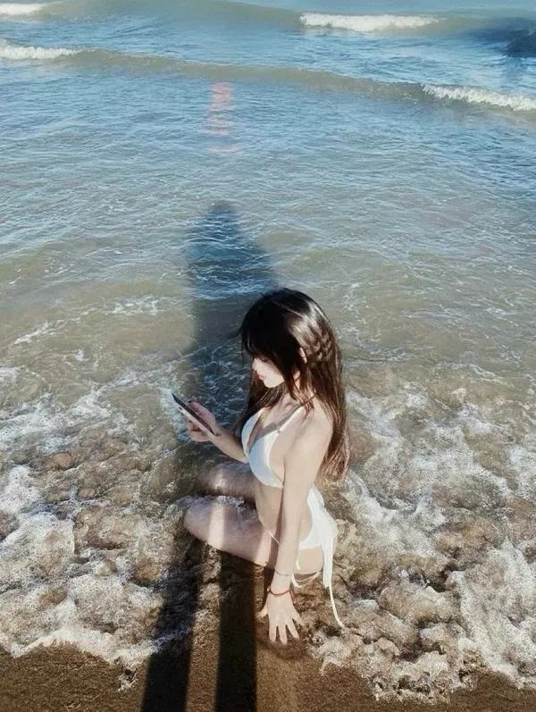 Gái đẹp đứng bên bờ đá lởm chởm mặc váy đen ngắn tay che tóc sau gáy nhìn xuống nước trong xanh.