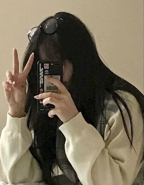 Giơ dấu peace một tay tay kia cầm điện thoại che mặt mặc áo trắng dài tay đầy tự nhiên.