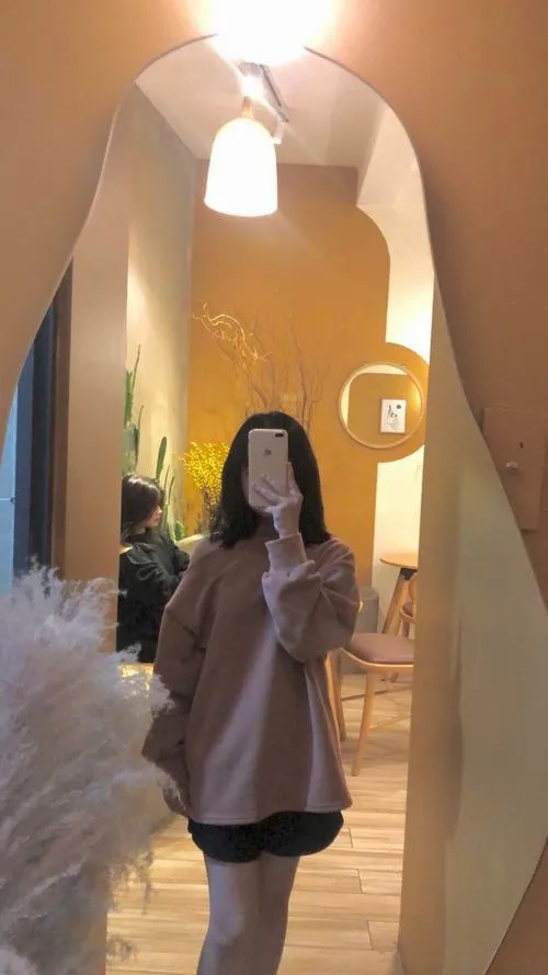 Đứng trong phòng ấm đèn vàng tóc dài áo nâu cầm điện thoại che mặt nhẹ nhàng.