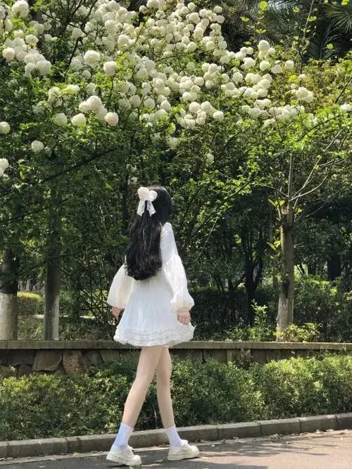 Gái đẹp mặc váy trắng ngắn đứng giữa vườn hoa trắng tóc dài buông xõa tự nhiên trong ánh sáng dịu.