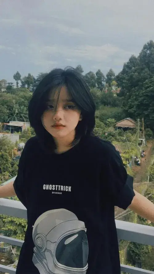 Ảnh gái mái tóc ngắn đen mặc áo thun đen rộng ngồi ngoài ban công ánh mắt cá tính hướng sang một bên.