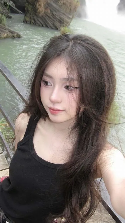 Gái xinh tóc nâu dài mặc áo tank đen nhìn thẳng camera nụ cười khẽ trong phòng ngủ ấm ảnh gái xinh TikTok Việt Nam.