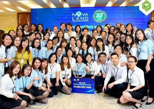 Ảnh nhân sự Novaland ngồi đông đủ trên bậc thềm trong đồng phục xanh trắng đồng bộ, ai cũng mỉm cười rạng rỡ tạo nên khung hình tập thể rất chuyên nghiệp