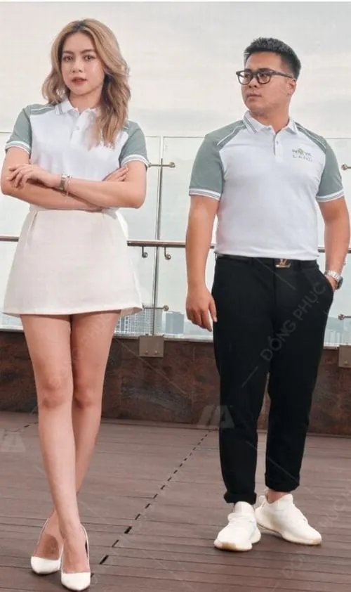 Cặp nam nữ đứng cạnh nhau trước nền sáng với áo sơ mi trắng và chân váy thanh lịch, dáng đứng thoải mái làm nổi bật vẻ trẻ trung của đội ngũ Novaland