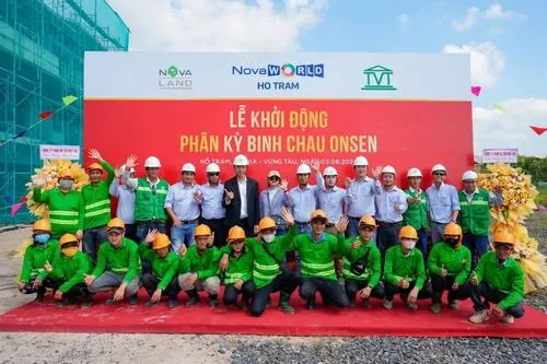 Khoảnh khắc tập thể đông người trên sân khấu sự kiện trong trang phục trang trọng, ánh đèn đỏ phía sau làm nổi bật không khí long trọng của sự kiện ra mắt
