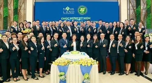 Đội ngũ nhân viên mặc vest đen đứng chụp ảnh trong hội trường sang trọng, biểu cảm tươi tắn cho thấy sự gắn kết của thành viên gia đình Nova