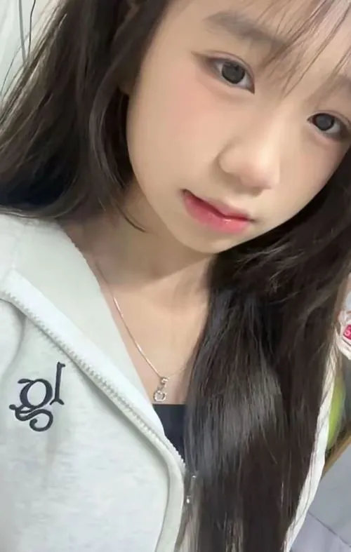 Ảnh gái cô nàng tóc dài đen chúm môi trong hoodie trắng, ánh mắt long lanh nhìn camera với vẻ tươi trẻ tự nhiên.