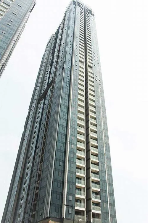 chung cư cao cấp tòa nhà vươn thẳng lên trời với lớp kính xanh phản chiếu mây trời, góc chụp từ chân lên tạo cảm giác hiện đại và luxury rõ nét