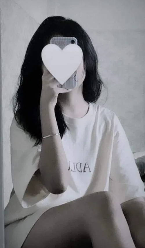 Thiếu nữ mặc váy midi hoa nhí tóc cột cao ngồi bên cửa sổ cầm điện thoại che mặt đón nắng vàng.