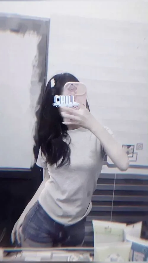 Gái đẹp mặc set đồ thể thao ôm sát tóc buộc đuôi gà đứng trước tủ kính dùng điện thoại che kín mặt.