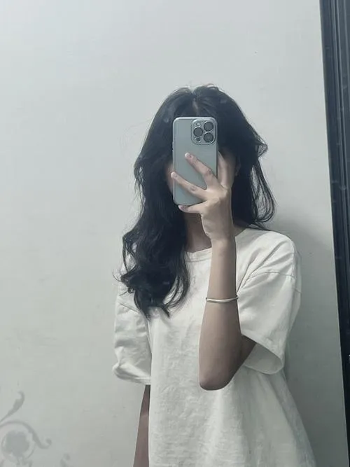 Gái xinh mặc váy da ngắn áo khoác denim tóc dài thẳng ngồi vắt chéo chân dùng điện thoại che mặt.