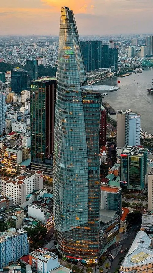 ảnh tháp tài chính góc nhìn từ trên cao thấy Bitexco nổi bật giữa cụm cao ốc, ánh chiều vàng phủ lên lớp kính xanh tạo cảm giác sang trọng và nhịp đô thị rõ rệt